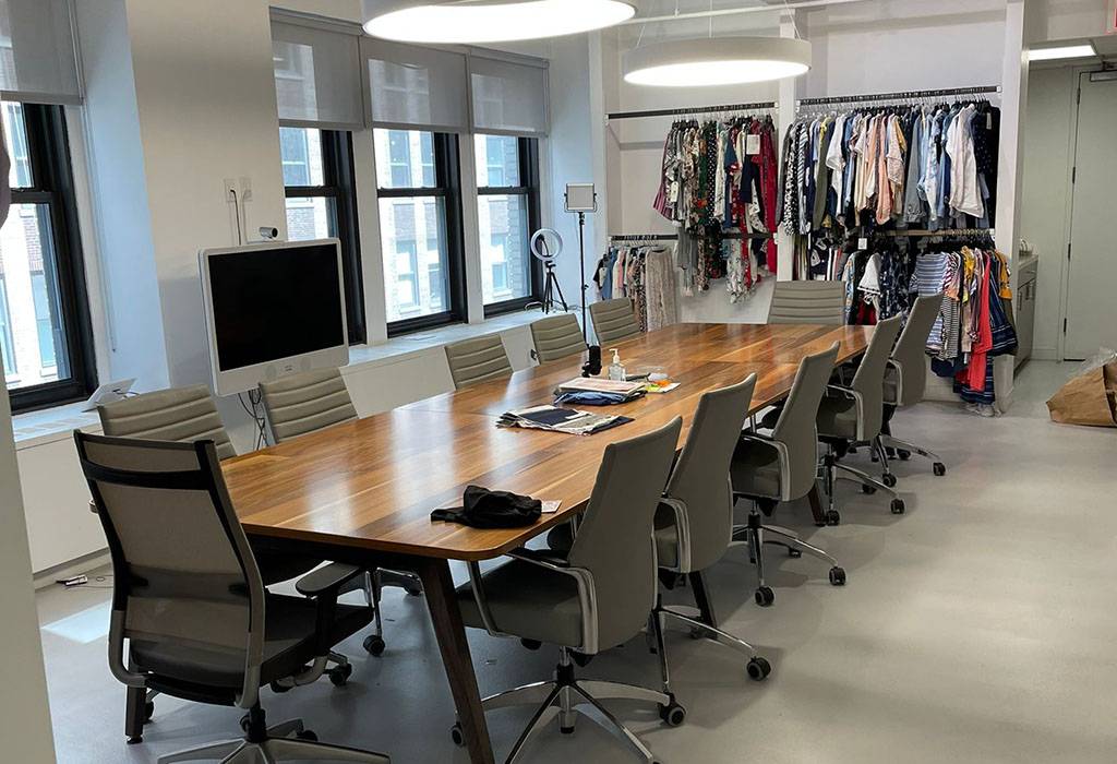 A room with a long table, chairs and clothing stands